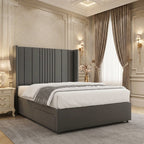 Dark grey upholstered divan bed with a tall winged headboard, broad vertical panels and narrow channel detailing.
