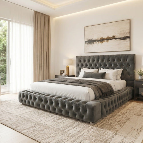 A modern bedroom featuring a dark gray tufted platform bed with a matching headboard, styled with white linens and a textured throw blanket, set on a distressed beige rug.